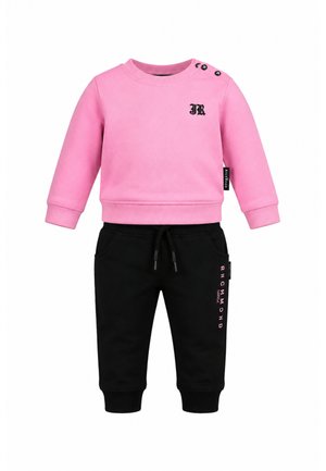 Felpa rosa a maniche lunghe con bottoni neri e pantaloni della tuta neri con scritta verticale rosa sulla gamba e vita con coulisse.