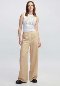 Top sin mangas blanco con adornos de cuentas, combinado con pantalones de pierna ancha beige. Textura suave, corte relajado y detalles de bolsillos laterales.