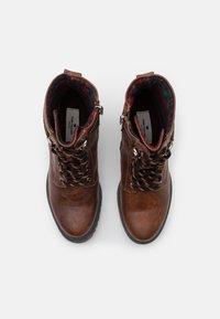 Stivaletti in pelle marrone con lacci neri e arancioni, fodera in fantasia tartan, punta arrotondata e zip laterale. Parte superiore testurizzata e suola in gomma.