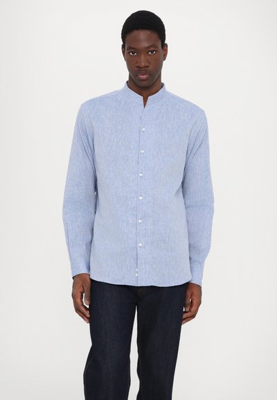 Ljusblå knappad skjorta med mandarin-krage, långa ärmar och en fin textur med ett subtilt mönster. Kombinerad med mörka jeans.