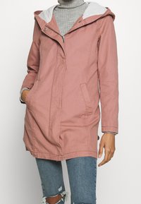 Jasnoróżowa kurtka zapinana na zamek z szarym kapturem i podszewką. Posiada dwie kieszenie z przodu oraz lekko zwężoną talię dla luźnego kroju.