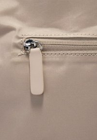 Lys beige taske med et tekstureret stof og en lynlåslukning. Lynlåsen har en sølvfarvet metaltræk og en matchende beige plastikdetalje.