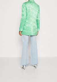 Un blazer verde con textura y un patrón de cebra vertical, combinado con jeans de campana azul claro y zapatos de tacón metálicos.