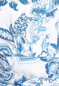 Tessuto bianco con un motivo floreale blu, caratterizzato da design intricati, bottoni e una consistenza liscia. I motivi includono foglie e spirali.