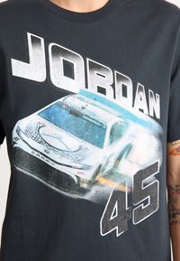 Camiseta de algodón negra con un gráfico de un elegante coche de carreras, con el texto "JORDAN" arriba y "45" abajo en letras blancas en negrita y desgastadas.