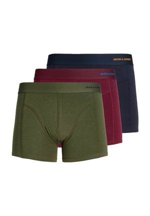 Jeune homme aux cheveux blonds courts portant un boxer vert olive Jack & Jones, debout devant un fond clair uni.