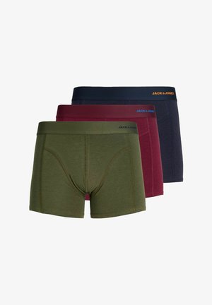 Noor mees lühikeste blondide juustega, kes kannab oliivrohelisi Jack & Jones bokserpükse, seisab ühetaustalise heleda tausta ees.