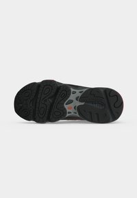 Μαύρη και γκρι σόλα παπουτσιού New Balance με υφής μοτίβα πέλματος και μικρό κόκκινο λογότυπο σε απλό φωτεινό φόντο.