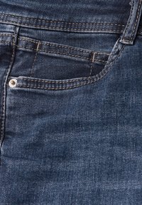 Los pantalones de mezclilla azul oscuro cuentan con un diseño clásico de cinco bolsillos, costuras visibles y un acento de botón de metal en el bolsillo delantero. Textura suave.