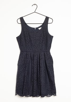 Robe noir sans manches en dentelle avec encolure ronde et taille cintrée, suspendue sur un cintre noir sur fond blanc.