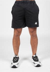 Zwarte denim shorts met een elastische band, zijzakken en een wit gorilla-logo aan de linkerkant. Gemaakt in combinatie met zwart-witte sportschoenen.