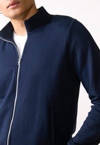 Marinblå zip-up jacka i slätt tyg, med hög krage och sidofickor, som har en formsydd silhuett och långa ärmar.