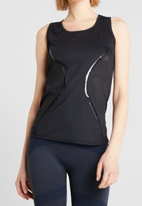 Svart atletisk linne med mesh-paneler, böjd design, slät textur och rund halsringning. Kombineras med mörka leggings med ribbade detaljer.