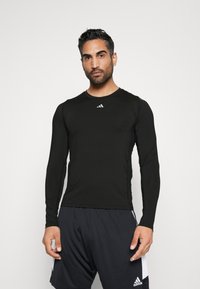 Schwarzes langärmliges Sportshirt aus glattem Stoff, mit rundem Ausschnitt und einem kleinen weißen Logo auf der Brust.