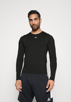 Schwarzes langärmliges Sportshirt aus glattem Stoff, mit rundem Ausschnitt und einem kleinen weißen Logo auf der Brust.