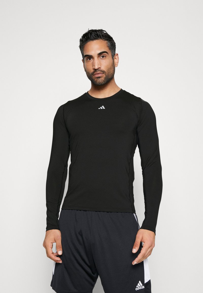Schwarzes langärmliges Sportshirt aus glattem Stoff, mit rundem Ausschnitt und einem kleinen weißen Logo auf der Brust.