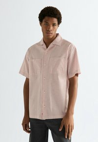 Πουκάμισο με κοντά μανίκια σε ανοιχτό ροζ χρώμα με λευκές κάθετες ρίγες. Διαθέτει γιακά τύπου camp, δύο μπροστινές τσέπες και κλείσιμο με κουμπιά.