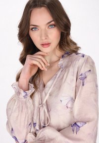 Lehká květinová blůza v jemné béžové barvě s fialovými vzory motýlů. Disponuje volánkovým výstřihem a nabíranými dlouhými rukávy s elastickými manžetami.