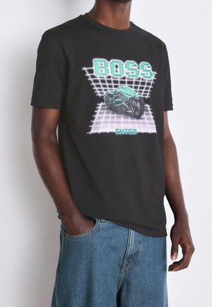 Mann trägt ein schwarzes T-Shirt mit neongrünem Schriftzug "BOSS" über einem futuristischen Motorrad und "ENTER" darunter vor einem Rasterhintergrund.