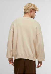 Pulover oversized de un bej deschis, cu tricot texturat, umeri lăsați și mansete și tiv bordurate. Design minimal, fit confortabil.