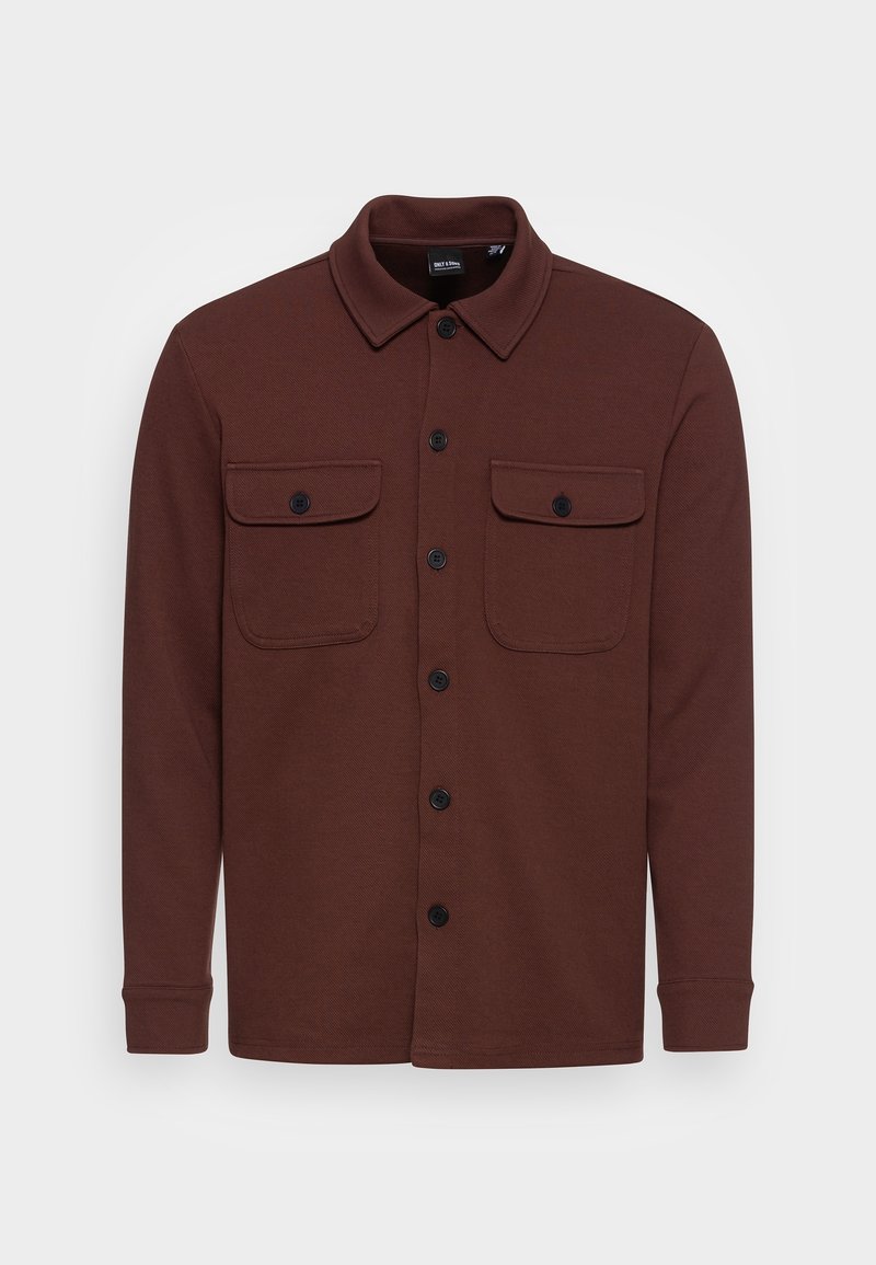 Bruine getailleerde blouse gemaakt van textuurstof, met een kraag, twee borstzakken en zwarte knopen. Lange mouwen met knoopsluitingen.