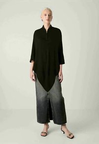 Musta korkea-alareunainen paita, jossa on neljännen osan vetoketju, yhdistettynä pitkään farkkuhameeseen, jossa on etuläppä, käytettynä nauhaketjuilla varustettujen sandaalien kanssa.