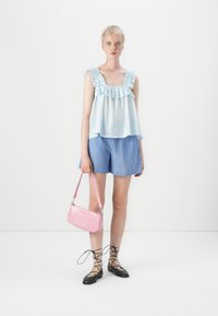 Lichtblauw mouwloos topje met een ruchesrand, gecombineerd met blauw gestreepte shorts. Het model houdt een roze handtas met krokodillenpatroon vast. Zwarte veterschoenen.