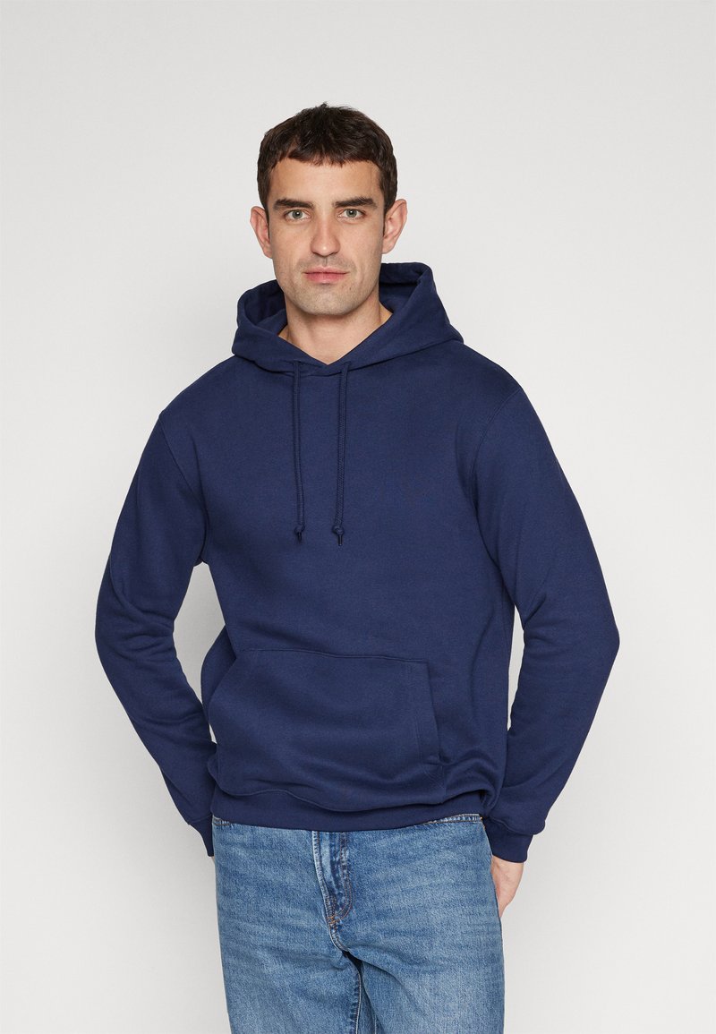Hanorac bleumarin dintr-un amestec de bumbac, cu un buzunar frontal tip kangaroo, sireturi la glugă și manșete ribbate. Purtați cu blugi de un albastru deschis.