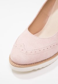 Chaussure en daim rose avec un bout arrondi, présentant des détails perforés et une semelle plateforme texturée. Doublure intérieure lisse, design décontracté.