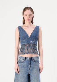 Top corto in denim con scollatura a V profonda, orlo con frange e cuciture tonali. Abbinato a pantaloni corti in denim a vita alta. Colore azzurro chiaro.