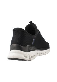 Chaussure de sport en mesh noir avec une semelle blanche rembourrée et des accents noirs. Présente une boucle au talon et un design ventilé pour la respirabilité.