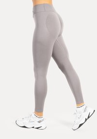Leggings grigio chiaro a vita alta con una texture liscia e un design aerodinamico. Presentano cuciture sagomate che valorizzano la forma, abbinati a sneakers bianche.