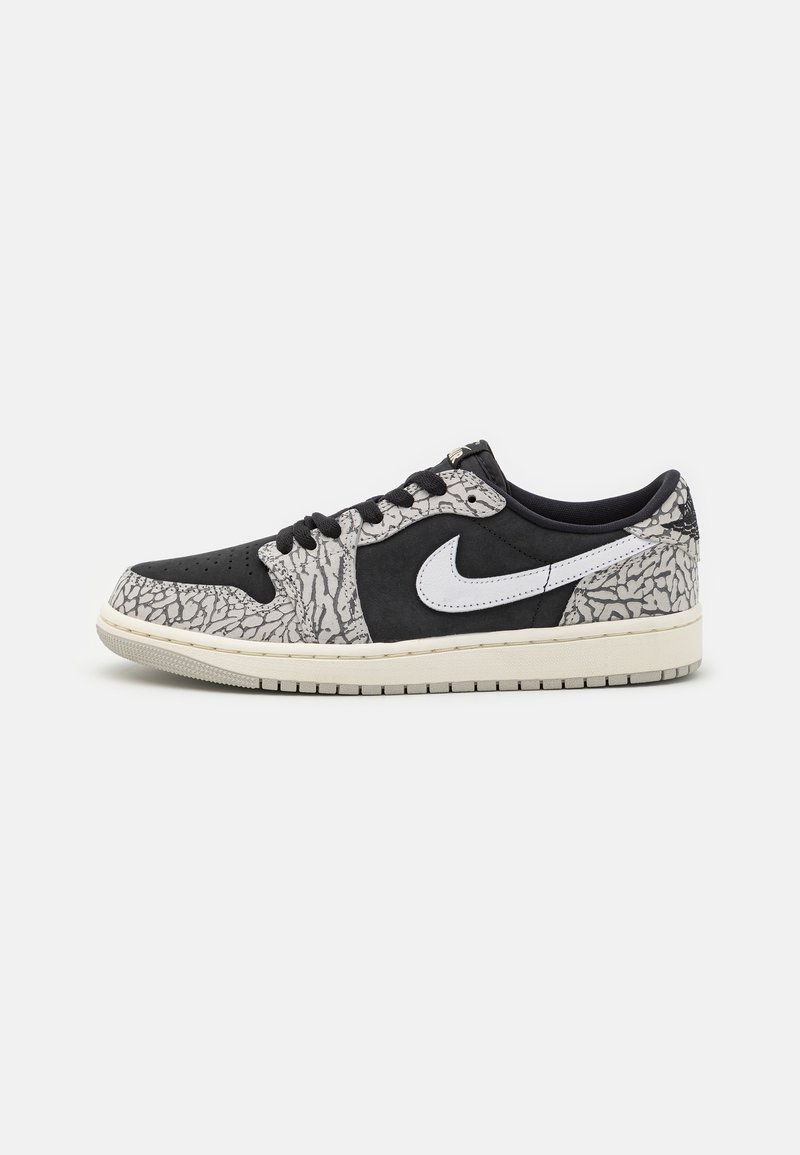 Basket basse noire et grise avec le logo blanc Nike, motifs béton craquelé, lacets noirs et semelle beige sur fond blanc.