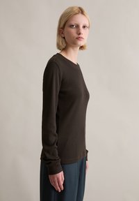 Haut marron à manches longues côtelées avec un col rond, une silhouette ajustée et une texture douce, associé à un pantalon bleu ample.