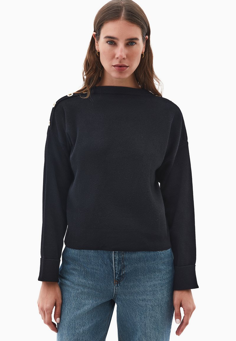 Schwarzer, gestrickter Pullover mit Rundhalsausschnitt, langen Ärmeln und goldenen Knopfakzenten an der Schulter. Das Material scheint weich und strukturiert zu sein.