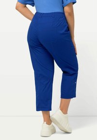 Pantalons courts bleus en tissu léger, dotés d'une taille élastique, de deux poches arrière et d'une coupe décontractée. Associés à des baskets blanches.