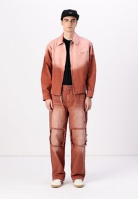 Rust-colored denim jacket with gradient effect, paired with ripped matching pants. Both feature a relaxed fit and minimal hardware details.