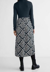 Šaty s dlouhým rukávem, s námořnickým topem a sukní se vzorem v geometrických krémových tvarech. Obsahují přiléhavý živůtek a splývavou spodní část.