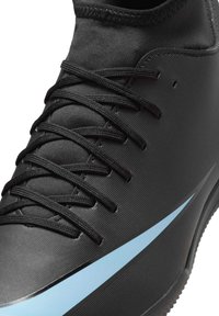Black athletic shoe with textured fabric, black laces, and a light blue swoosh logo on the side, shown in close-up detail.
