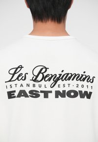 T-shirt blanc avec texte brodé noir : "Les Benjamins," "ISTANBUL EST. 2011," et "EAST NOW" dans différentes polices et tailles.