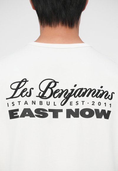 Valge T-särk, millel on musta tikandiga tekst: "Les Benjamins," "ISTANBUL EST. 2011" ja "EAST NOW" erinevates fontides ja suurustes.