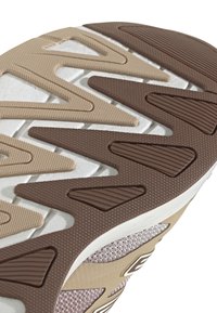 Potplat cipele s raznolikim uzorkom u obliku cik-caka, izrađen od smešane smeđe i bež gume, sa teksturiranim površinama i belim srednjim delom. Izdržljiv i osmišljen za dobru prionljivost.