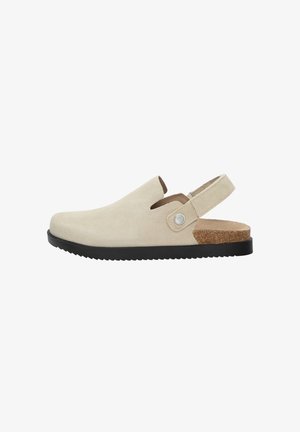 Bež nubuk cipele slip-on s otvorenom petom, crnim gumenim potplatom, plutenim detaljem na peti i malim kružnim hardverskim detaljem sa strane.