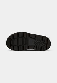 Suela de zapato de goma negra con superficie texturizada, que presenta patrones de banda de rodadura multidireccionales y un área de punta suave. Sin marcas visibles.