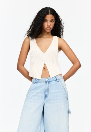 Cream ribbed vest top with a V-neck and front buttons, paired with light blue wide-leg jeans featuring side pockets and a relaxed fit.