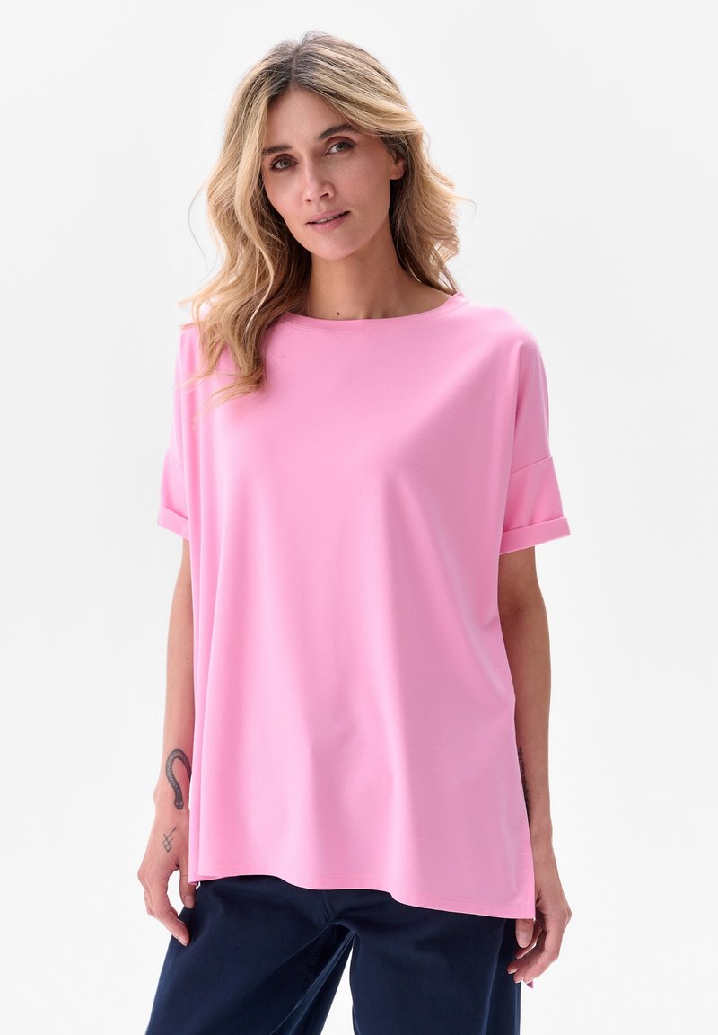 Jasnoróżowa bluzka z krótkim rękawem, okrągłym dekoltem, luźnym fasonem oraz podwiniętymi rękawami; miękka tekstura i casualowy styl.