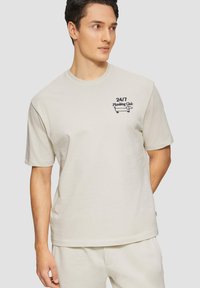 Lichtbeige katoenen t-shirt met korte mouwen, ronde halslijn en geborduurd logo "24/7 Planking Club", voorzien van een eenvoudig, casual ontwerp.