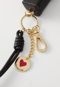 Black leather keychain with gold hardware, featuring a red heart charm on a round pendant inscribed with "Lovel Moschino." Chain accent included.
