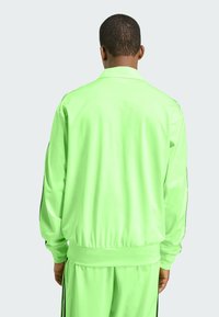 Neon groene trainingsjack met een gladde textuur, voorzien van een kraag, elastische manchetten en zwarte zijstrepen op de mouwen.