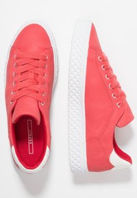 Baskets basses rose corail avec semelles en caoutchouc blanches, lacets assortis roses, et un accent blanc au talon, vues de dessus et de côté.